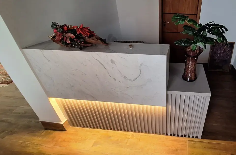 Balcão de recepção revestido em pedra clara, com luz embaixo