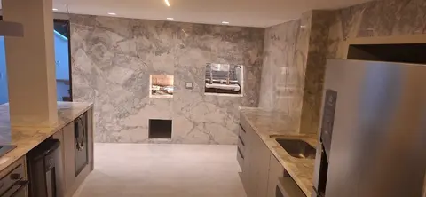 Área gourmet com parede e churrasqueira revestidas em pedra de veios cinza