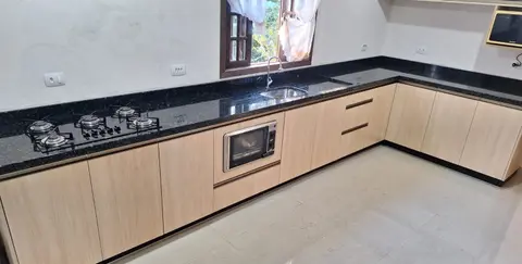 Cozinha em L com bancada de granito preto, cooktop e cuba