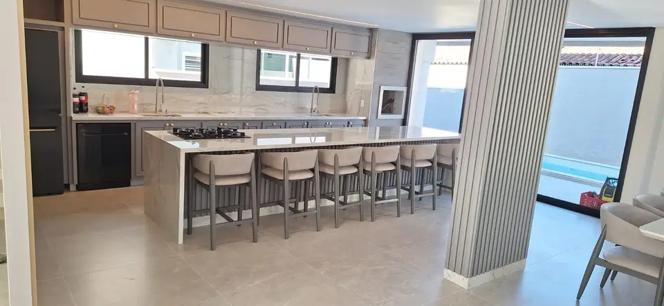 Ilha de cozinha em pedra clara com a lateral até o chão e oito banquetas